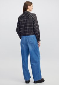 Camicia a quadri nera e marrone, tagliata, con maniche lunghe, abbinata a pantaloni in denim azzurro chiaro, larghi. Ai piedi, calzature chunky nere.