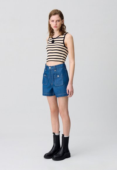 Top corto de punto a rayas en beige y negro, combinado con pantalones cortos de mezclilla de tiro alto en azul con bolsillos frontales, y botas negras hasta el tobillo.