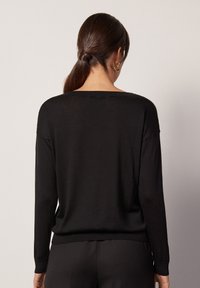 Pull noir à manches longues avec un large décolleté et des poignets côtelés. Tissu en maille douce et légère, avec une coupe décontractée et une texture lisse.