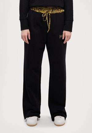 Black sweatpants with a yellow patterned waistband, featuring a drawstring and side logo detail. Smooth texture with a straight leg design.