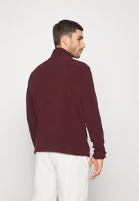 Pullover in pile bordeaux con colletto alto, maniche lunghe e una texture liscia. Presenta una vestibilità comoda e un orlo dritto.