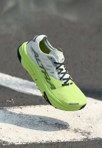 Chaussure de course avec une tige en maille jaune-vert vif, des accents gris et des lacets noirs. Présente une semelle rembourrée et un motif texturé pour une meilleure adhérence.