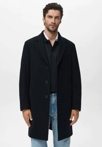 Palton navy din lână cu guler decupat, design cu un singur rând de nasturi și două buzunare frontale. Purtați peste un polo negru și blugi blue.