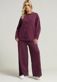 Burgundy lounge-set med en knapframsydd topp med långa ärmar och vida byxor. Mjuk tyg med minimal textur.