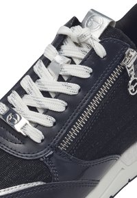 Baskets navy présentant un mélange de tissu texturé et de cuir lisse, lacets blancs, détail de fermeture éclair argenté et semelle à motifs.