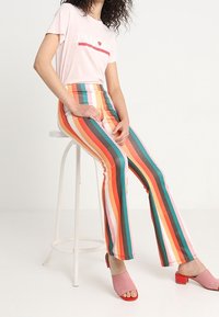Camiseta rosa clara con gráfico, combinada con pantalones de campana de rayas multicolores de cintura alta. El modelo lleva zapatillas de tacón abiertas rosas.