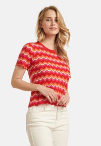 Rood en oranje zigzagpatroon korte mouw gebreide top met een ronde hals, textuurstof en een cropped ontwerp, gecombineerd met witte broek.