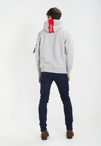 Felpa grigia con logo rosso sul cappuccio, con coulisse regolabile, polsini a costine e vita a costine, indossata con pantaloni skinny blu scuro.