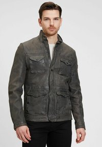 Graue Lederjacke mit Stehkragen, mehreren Fronttaschen, strukturiertem Finish und sichtbaren Nähten. Mit Reißverschluss.