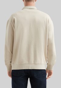 Felpa beige con colletto, maniche lunghe, polsini e orlo a costine, e una texture pulita e liscia. Design minimalista senza motivi visibili.