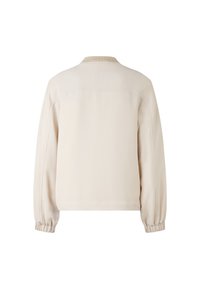 Jasno beżowa kurtka o luźnym kroju, z prążkowanym kołnierzem iElastycznymi mankietami. Gładki materiał o minimalistycznym wzornictwie, bez widocznych zapięć.