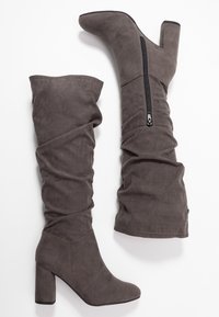 Bottes grises montant au-dessus du genou en daim souple, avec un design décontracté, une fermeture éclair latérale et un talon épais pour un bon maintien.