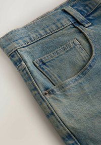 Jean en denim bleu plié, montrant la poche arrière, la passants de ceinture, le rivet et la texture décolorée du tissu sur un fond clair.