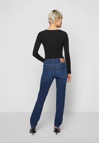 Jeans de ganga azul escuro com corte straight-leg e dois bolsos traseiros, combinados com uma blusa preta de manga longa ajustada.