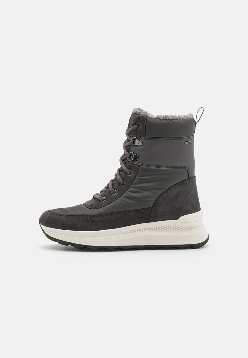 Botas altas en negro y gris que presentan una mezcla de cuero liso y ante, con forro de piel en la parte superior y una suela blanca acolchada.