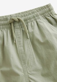 Lysgrønne shorts med elastisk talje, snørelukning og diskrete syninger. Stoffet ser glat ud med en let mat overflade.