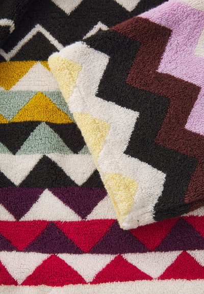 Πολύχρωμες πετσέτες μπάνιου με σχέδιο σε ζικ-ζακ σε μαύρο, άσπρο, κίτρινο, πράσινο, μοβ και κόκκινο, φτιαγμένες από μαλακό, υφασματιστό υλικό.