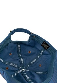 Gorra de mezclilla azul con corona cosida, ojales marrones, forro interior con el logo repetido "LOIS JEANS" y una asa superior para llevar.