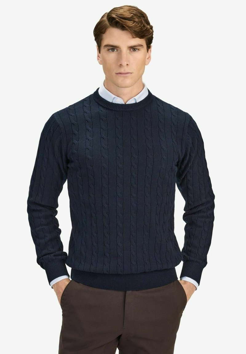 Tummansininen neulepaita, jossa on käärmeennahkakuvio, ribbaus kauluksissa, hihoissa ja helmassa. Päällä vaaleansininen kauluspaita, joka esittelee teksturoitua kangasta.