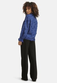 Blue embroidered blouse with long sleeves, featuring floral patterns and gathered accents at cuffs, paired with wide black trousers.