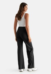 Pantaloni larghi neri con vita alta, abbinati a una canotta bianca. Presentano un tessuto morbido e una silhouette pulita.