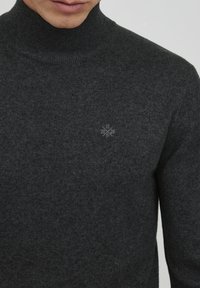 Pulover turtleneck de culoare gri închis, confecționat dintr-un material tricotat cu striații, având un logo subtil imprimat pe piept. Textură netedă, design ajustat.