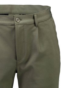 Lähikuva oliivinvihreistä housuista, joissa on nappikiinnitys, vyölenkit ja sivutasku, esittäen kangaspinnan tekstuuria ja ompelun yksityiskohtia.