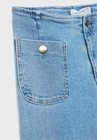 Détail d'un jean en denim bleu clair montrant une poche avant avec un bouton argenté et des coutures visibles sur un fond uni.