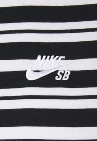 Black and white striped t-shirt with cotton fabric; features an embroidered Nike SB logo in white on the center, showcasing a clean design.