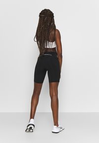 Sort træningsshorts og en hvid cropped top. Shortsen har en tætsiddende pasform og er i midt-lår længde. Hvide sneakers er synlige.