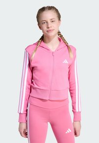 Sudadera rosa con cremallera, con rayas blancas en las mangas y un pequeño logo en el pecho, hecha de una tela suave y con un diseño corto.