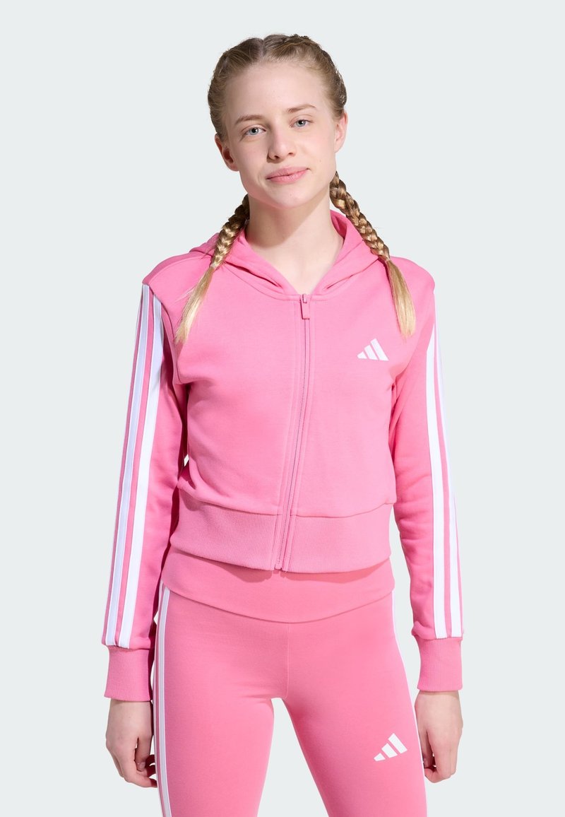 Sudadera rosa con cremallera, con rayas blancas en las mangas y un pequeño logo en el pecho, hecha de una tela suave y con un diseño corto.