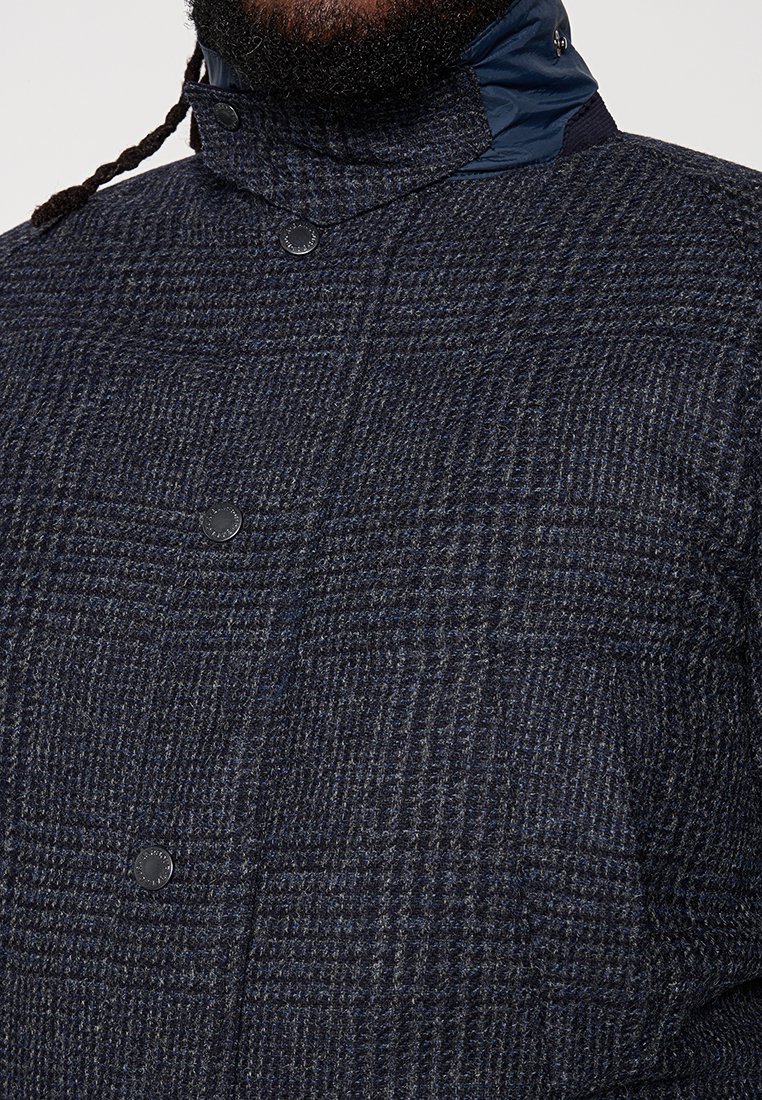 Navy karierten Mantel aus strukturiertem Wollmaterial mit einem hohen Kragen, Knopfverschlüssen und Stoffakzenten am Hals für zusätzliche Wärme.