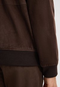 Bruine suède jacket met een gladde textuur, voorzien van een ribgebreide tailleband en manchetten, ontworpen met een eenvoudige, strakke silhouet.