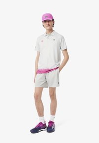 Polo shirt gris claro con un diseño de degradado rosa, pantalones cortos a juego, una gorra rosa y zapatillas deportivas moradas con acentos blancos.
