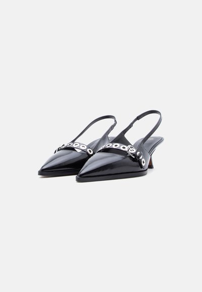 Μαύρα slingback τακούνια από δερμάτινο βινύλιο με μυτερές μύτες και λουριά διακοσμημένα με ασημένιες τρύπες μπροστά, σε λευκό φόντο.