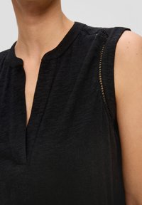 Black sleeveless top with a v-neck, featuring subtle texture and a sheer accent at the shoulder seam. Fabric appears soft and lightweight.