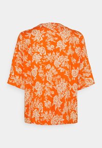 Haut à manches courtes orange à la coupe ample. Présente des motifs floraux de couleur crème et une texture lisse. Encolure arrondie.