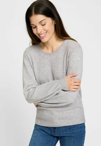 Hellgrauer Pullover aus weichem Material, mit Rundhalsausschnitt, langen Ärmeln und gerippten Bündchen, kombiniert mit blauen Jeans.