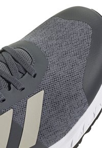 Grey athletic shoe featuring a textured mesh upper, smooth gray accents, and a white outsole with a black tread pattern.