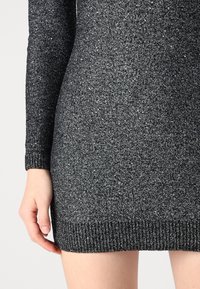 Black and silver speckled knit dress with long sleeves, ribbed cuffs, and hem. Close-up shows texture and material details.