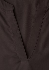 Tmavě hnědá látka s výstřihem do tvaru písmene V a viditelnými švy kolem oblasti límce.