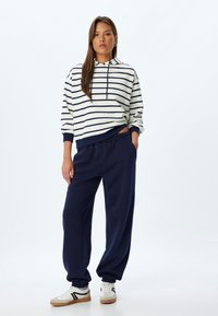 Gestreepte hoodie in crème en marineblauw, met een trekkoordcapuchon. In combinatie met marineblauwe joggingbroek met een elastische tailleband en aangeknoopte manchetten.