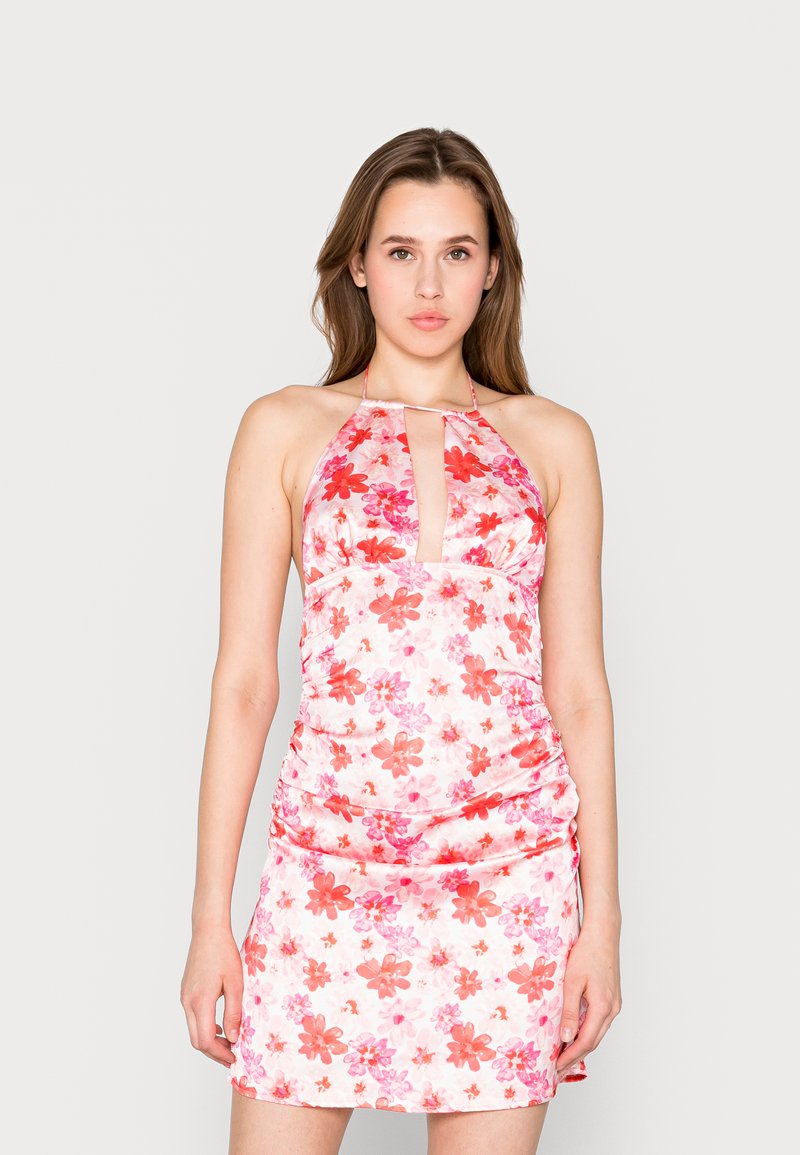 Vestido mini floral com decote halter, apresentando um recorte em forma de chave, tecido rosa com flores vermelhas e rosas em mistura, e detalhes franzidos nas laterais.