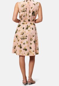 Blumenkleid aus leicht rosa Stoff, mit einer taillierten Taille, ärmellosem Design und elastischem Rücken. Akzentuiert mit grünen und schwarzen Blumenmustern.