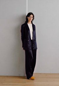 Sacou din catifea neagră cu nasturi dubli, asortat cu pantaloni negri pe măsură. Ținuta este completată de un top alb și adidași galbeni.