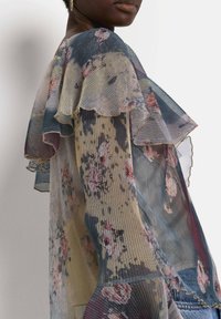 Floral pleated fabric blouse featuring ruffled sleeves in pastel shades of blue, pink, and cream, with sheer texture and layered design.