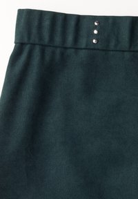 Tissu texturé vert foncé avec une large ceinture comportant trois boutons métalliques sur le devant. Le tissu présente un motif côtelé subtil.