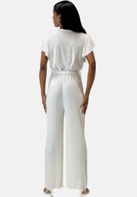 Pantaloni bianchi a pieghe ampia con vita aderente, abbinati a una blusa corta a maniche corte ampia, che mostrano un tessuto morbido e un design minimalista.