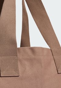 Κοντινό πλάνο των λαβών καφέ υφασμάτινης τσάντας tote, ραμμένες με ενισχυμένη ραφή πάνω σε υλικό από υφή καμβά.